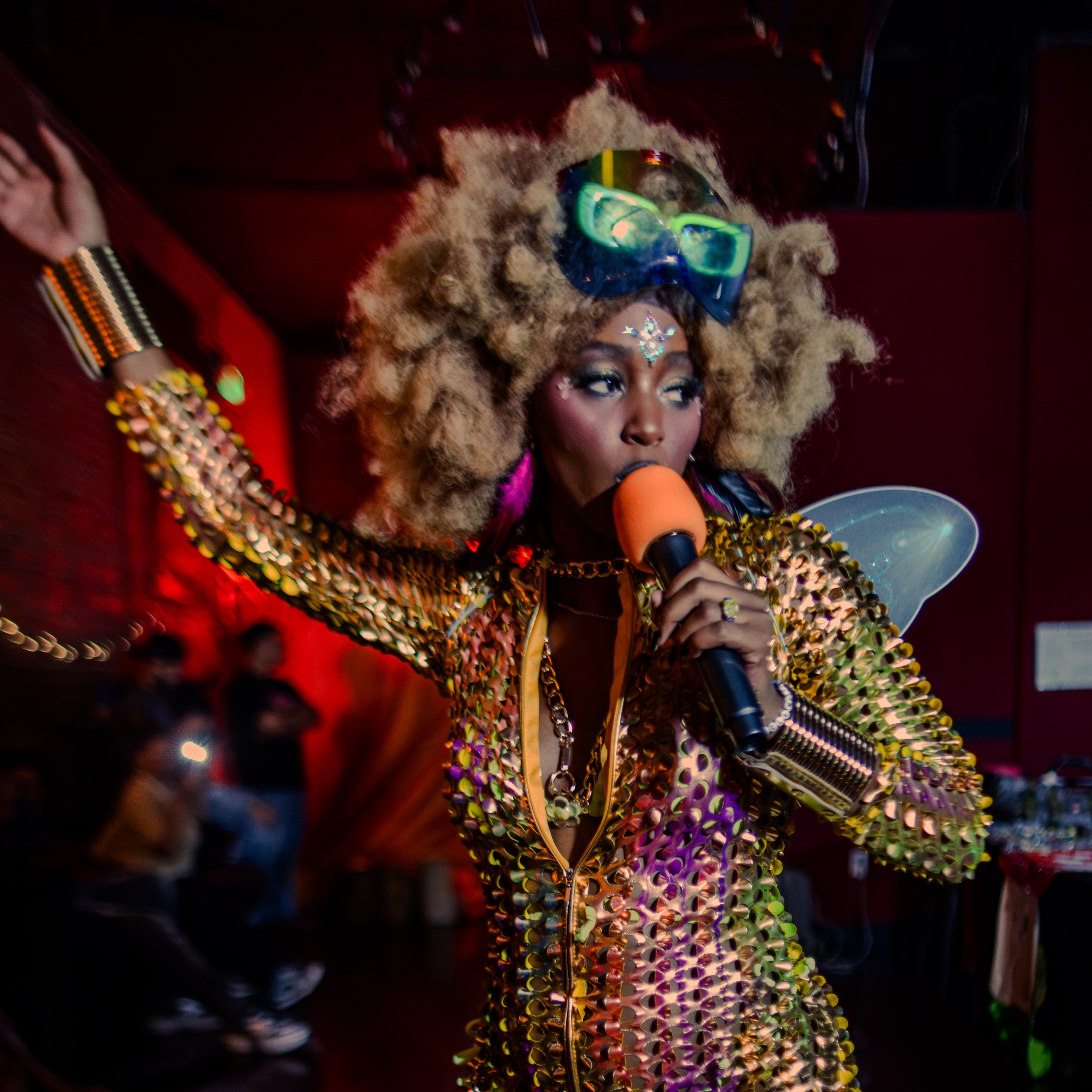 Neferttiti performing with a microphone in a gold look at Mushroom Dreams